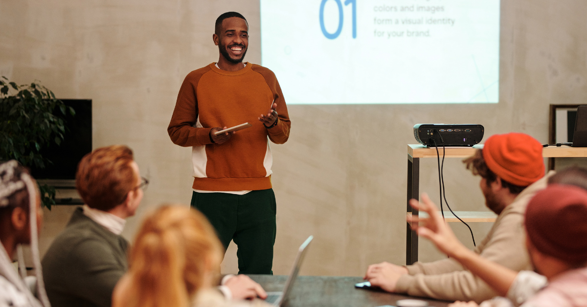 Man in Brown Crew Neck T-shirt Standing in Front of People at event presenting