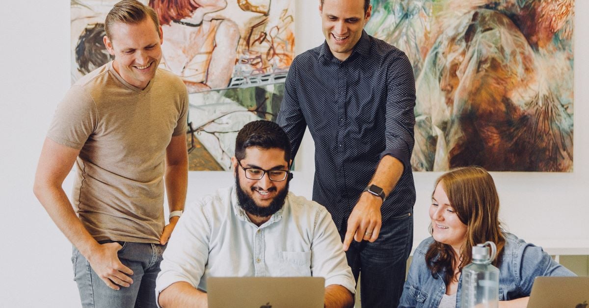 Coworkers engage with each other around a laptop